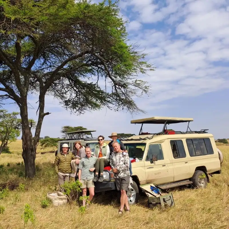 Safari guests with guide beside Land Cruiser in open savannah